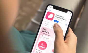 A woman's hand holding a smartphone and looking at a period and ovulation tracker